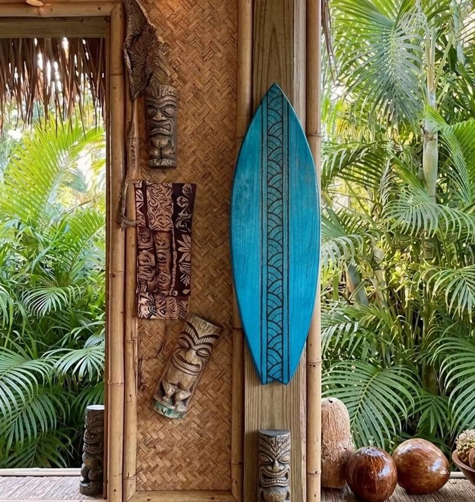 Glossy ocean-blue wooden fish-tail surfboard with a hand-carved Polynesian wave-pattern stringer in a tropical lanai